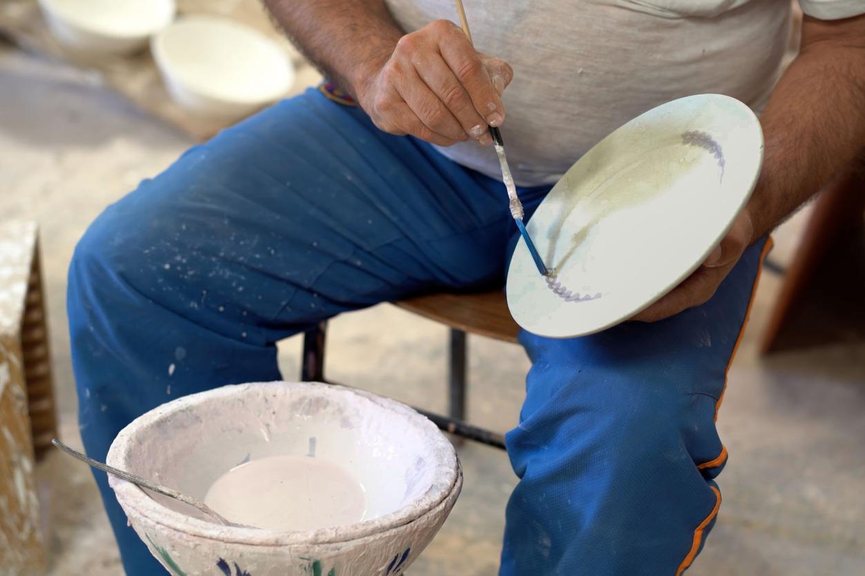 A kashigar painting a freehand motif onto an unfired plate