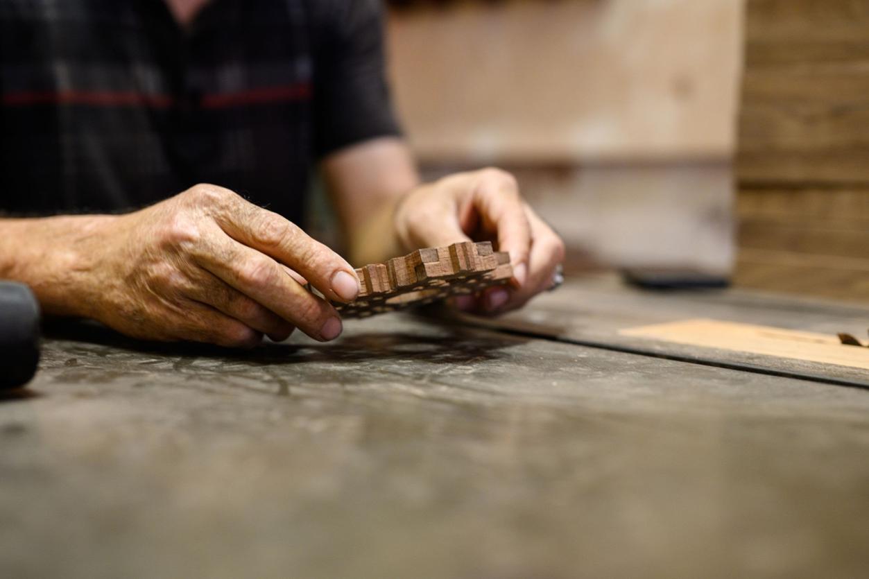A craftsman's hands holding a small carved wooden lattice panel